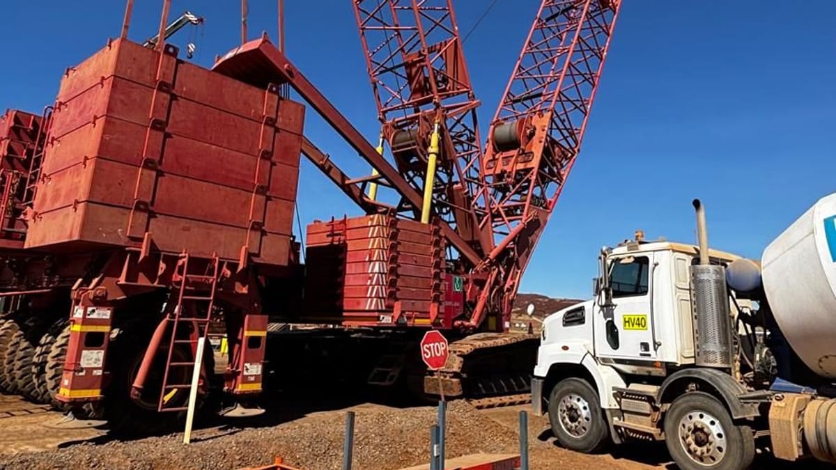 Crawler crane rigged with counterweights beside a concrete agitator on a remote site